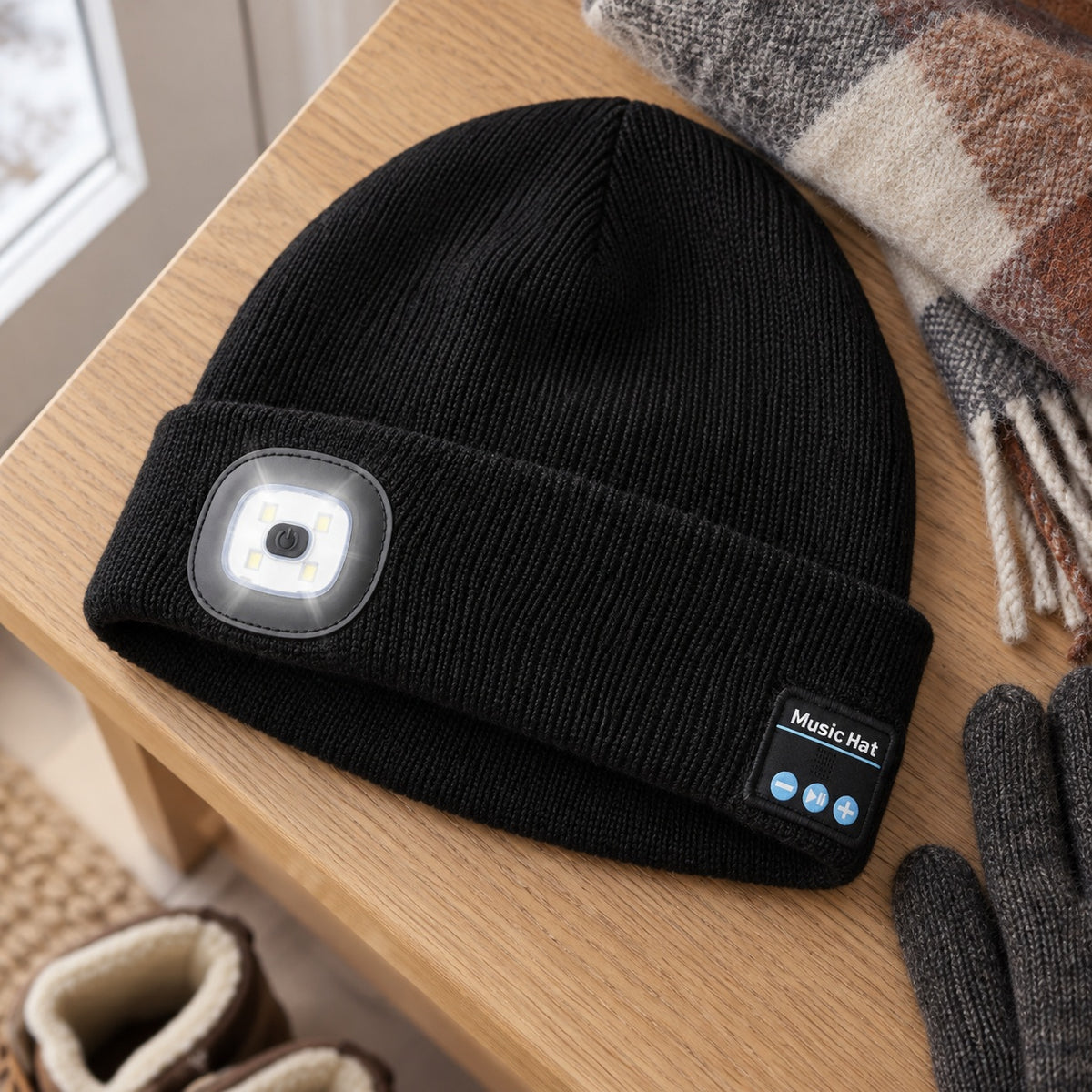 Svart strikket lue med LED-lykt foran og Music Hat-knapper på siden, ligger på en eikebenk