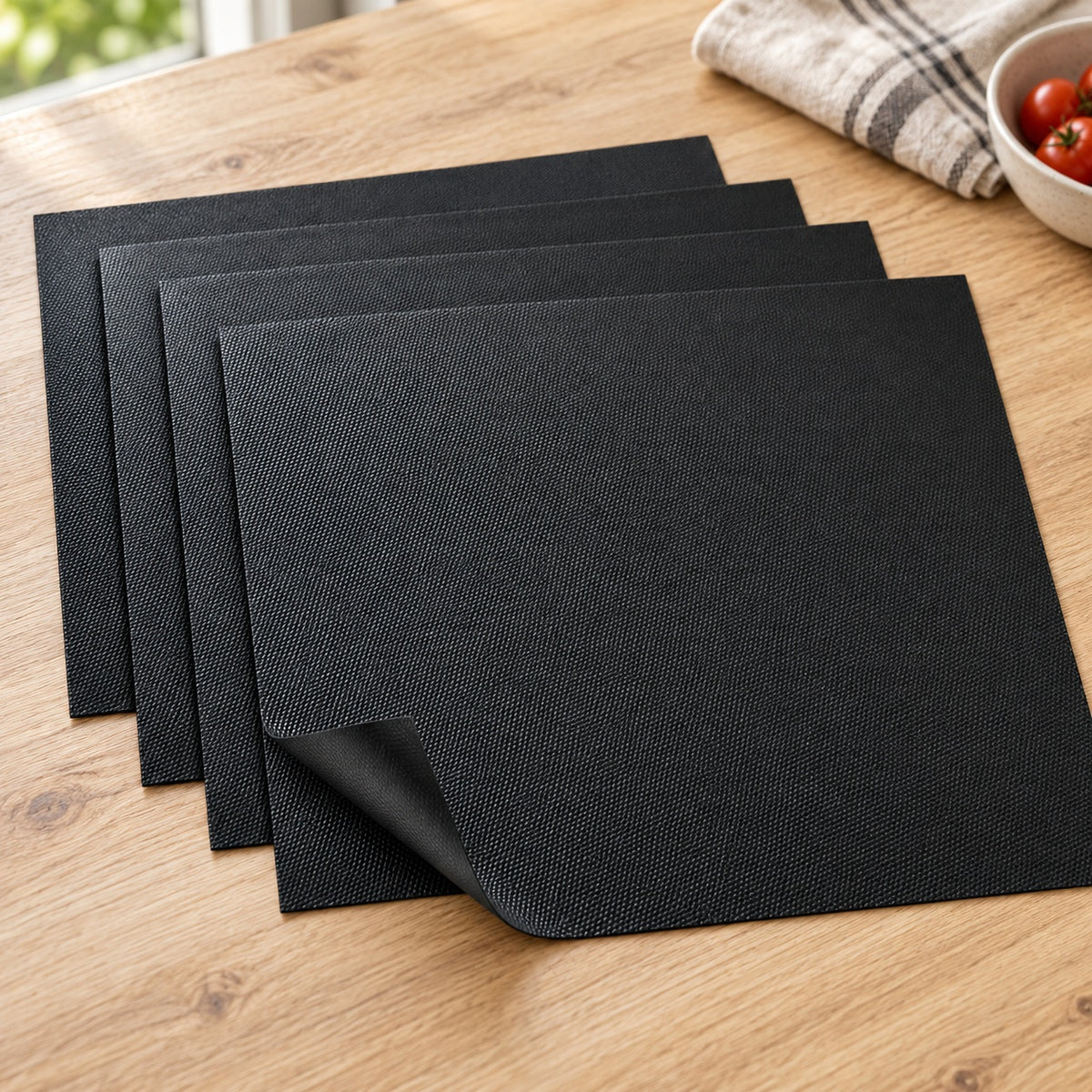 Four black Grill&Chill BBQ mats fanned out on an oak table